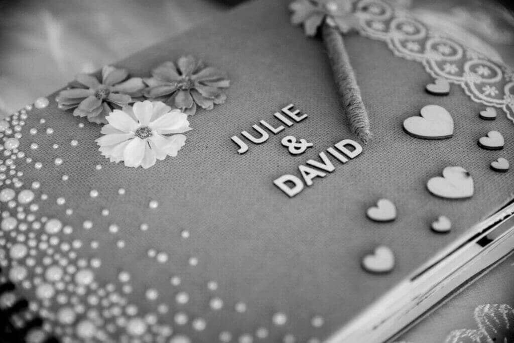 Livre de mariage personnalisé en noir et blanc avec les noms 'JULIE & DAVID' entourés de cœurs et de fleurs.