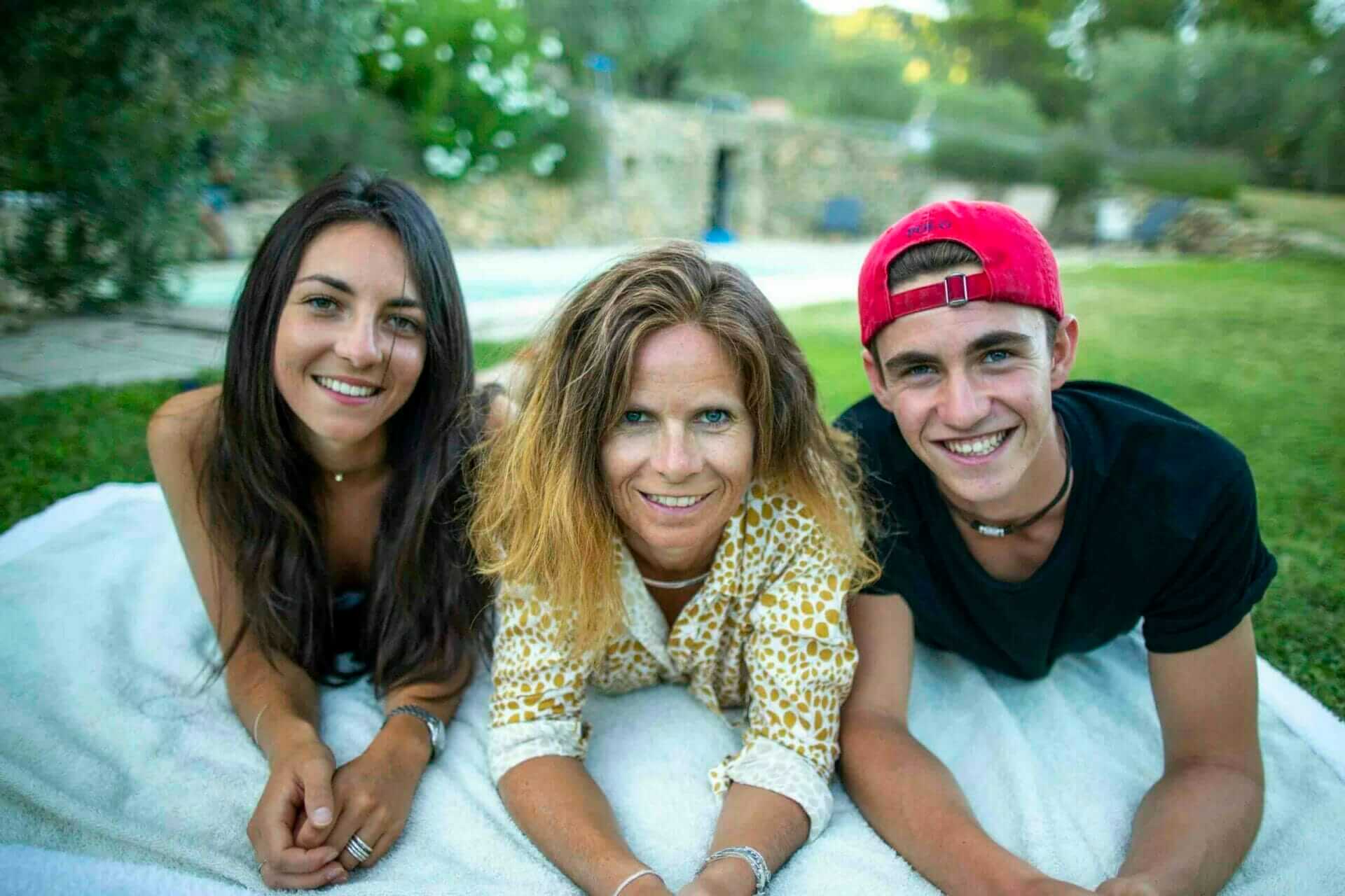 Une mère et ses deux enfants, souriants et allongés sur une couverture, lors d'une séance photo en extérieur avec un photographe.