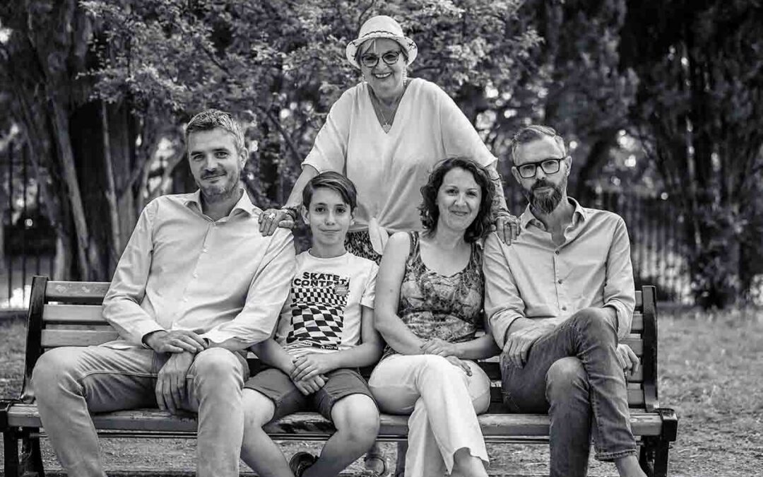 Portrait en noir et blanc d'une famille souriante assise sur un banc dans un parc, immortalisé par un photographe lors d'un shooting photo.