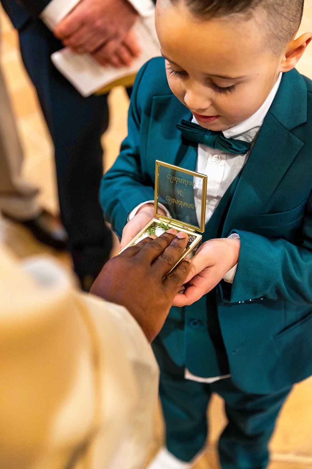 Rôle Précieux - Porteur d'Alliance en Mission Garçon d'honneur en costume vert tenant avec soin la boîte des alliances lors d'une cérémonie de mariage.