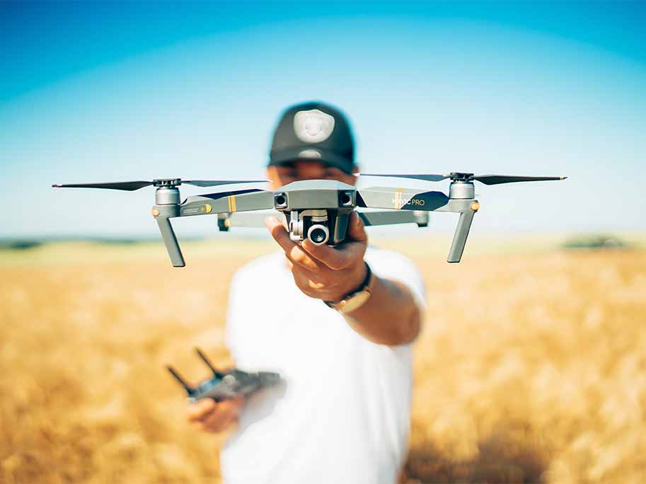 Drone 17 Photographie d'un pilote tenant un drone professionnel avec caméra dans un champ de blé sous un ciel bleu clair, illustrant la précision du pilotage de drones.