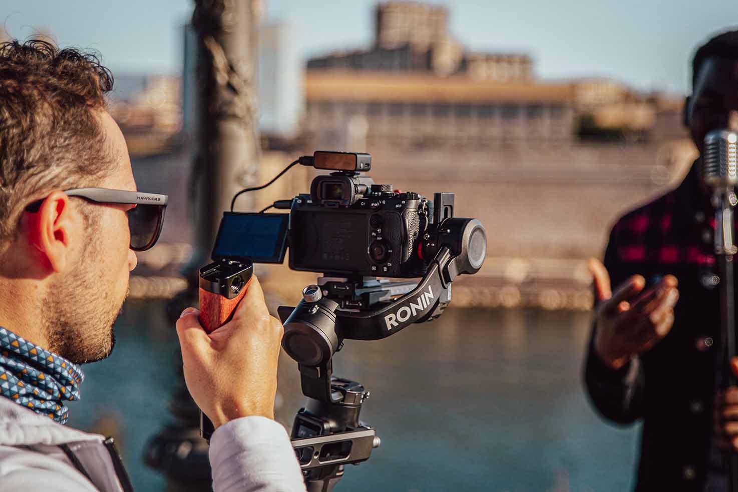 Vidéaste professionnel utilisant un stabilisateur de caméra Ronin pour filmer en extérieur, avec un sujet flou en arrière-plan.