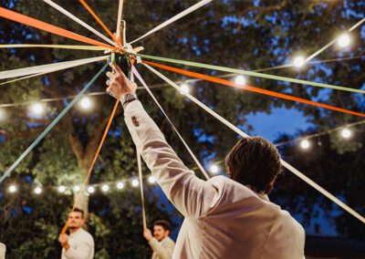 Photo, vidéo et duo photo + vidéo pour votre mariage à Aix-en-Provence 7 Le marié lève une bouteille au centre d’une animation de soirée sous des rubans colorés et des guirlandes lumineuses