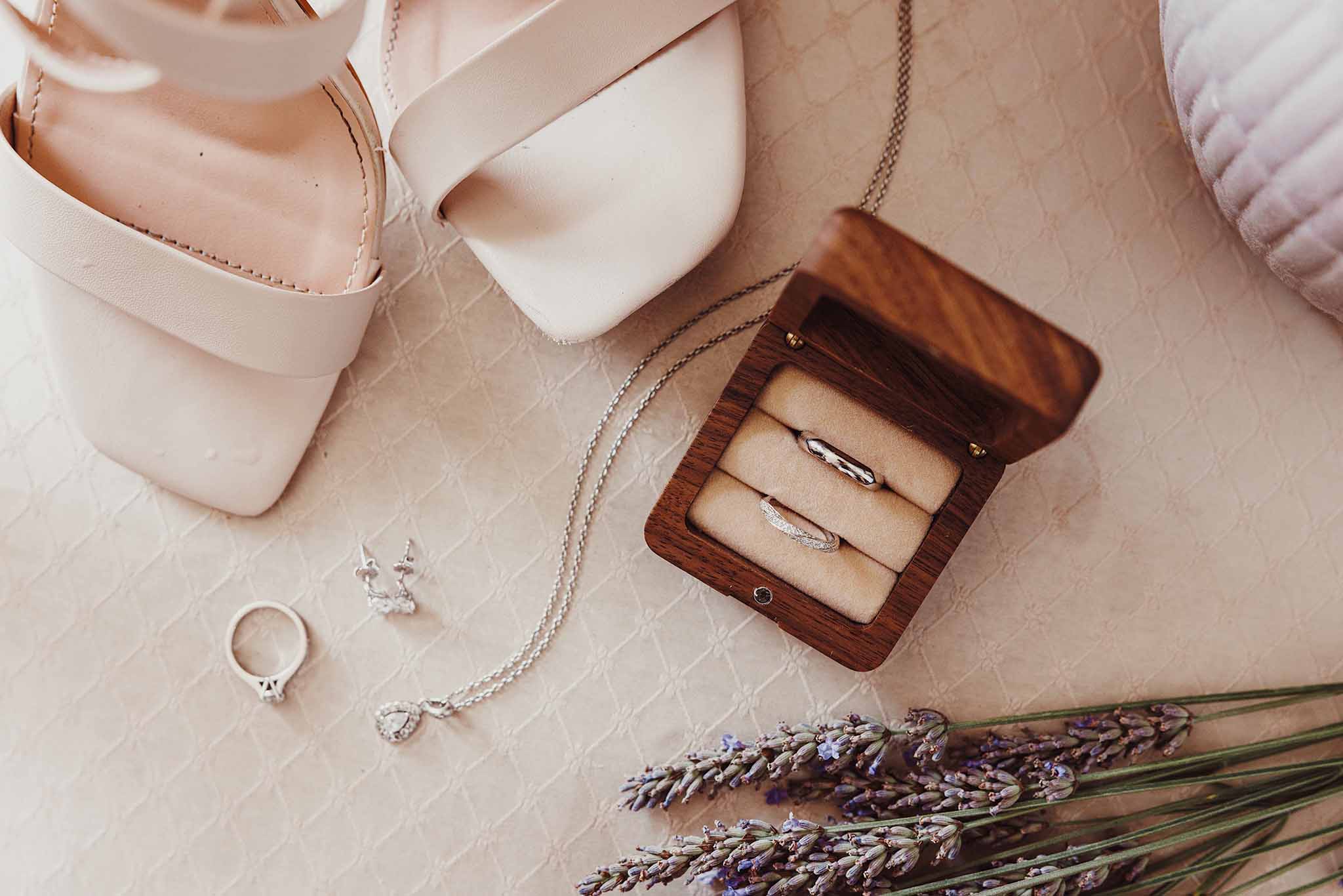 Boîte à alliances en bois ouverte avec bijoux et chaussures de la mariée posés sur un tissu clair