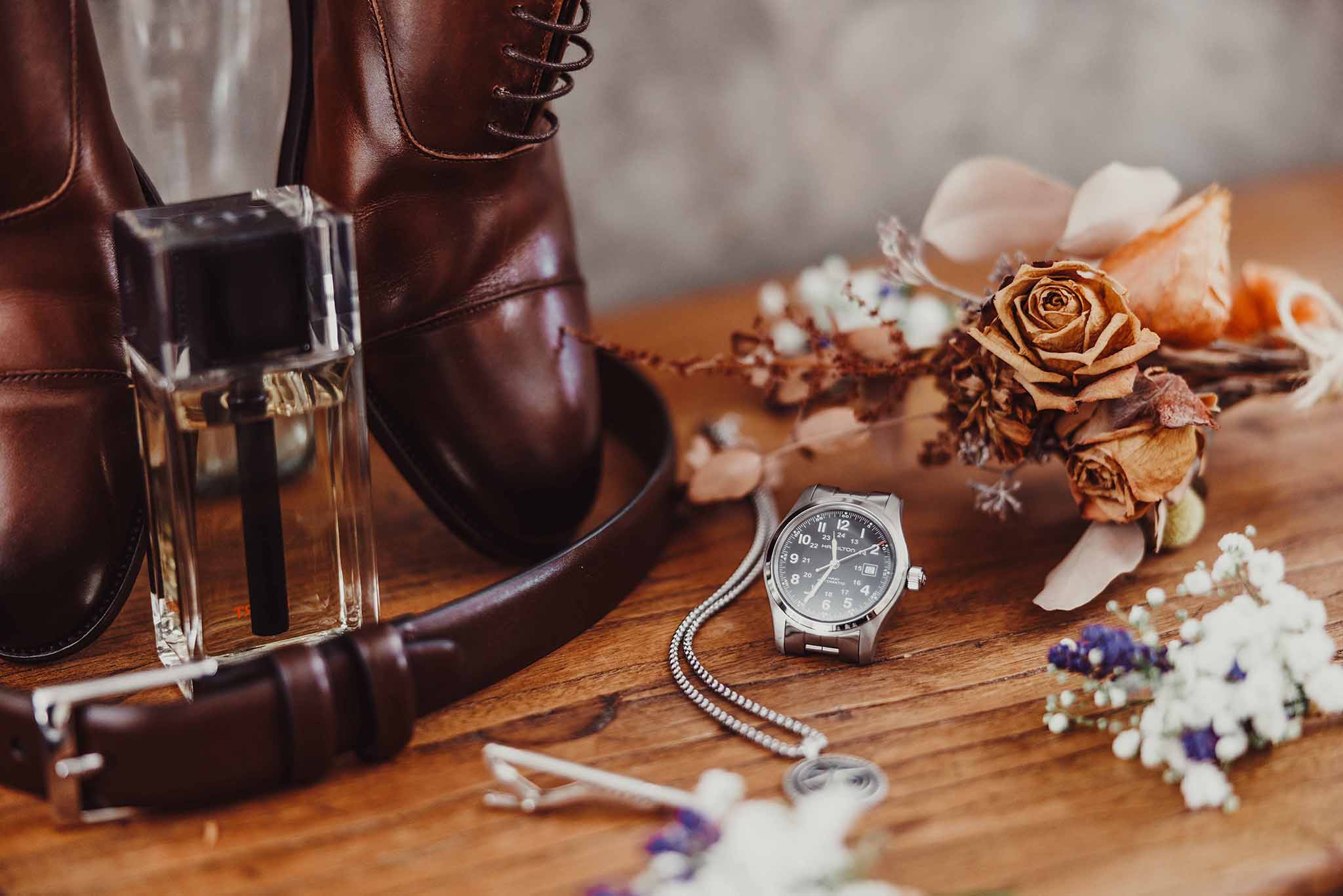 Chaussures en cuir du marié avec montre, parfum et accessoires posés sur une table en bois