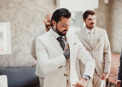 Photo, vidéo et duo photo + vidéo pour votre mariage à Aix-en-Provence 16 Le marié ajuste sa veste blanche entouré de ses proches pendant les préparatifs