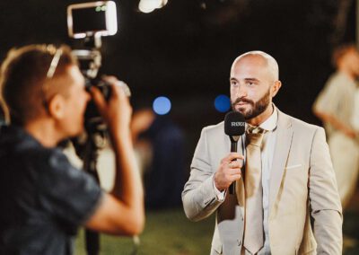 Un invité parle dans un micro pendant qu’un vidéaste le filme durant la soirée de mariage