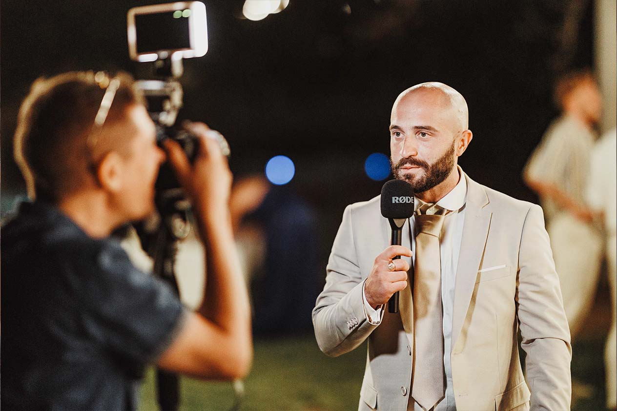 Message vidéo d’un invité pendant la soirée Un invité parle dans un micro pendant qu’un vidéaste le filme durant la soirée de mariage
