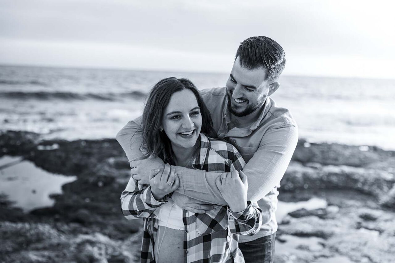 Photographe grossesse Martigues : couple riant en noir et blanc face à la mer
